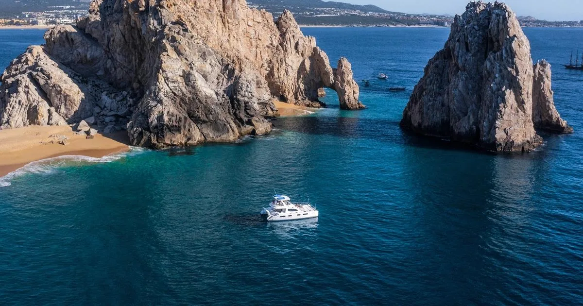 Aerial view of a white boat in deep blue water near the rock arch at Land's End, Cabo San Lucas