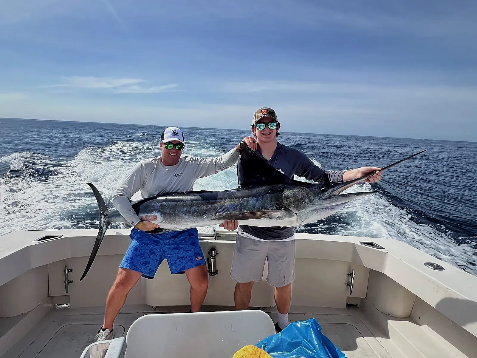 Two anglers holding a marlin across the stern of a boat with the wake and open ocean behind them in Los Cabos