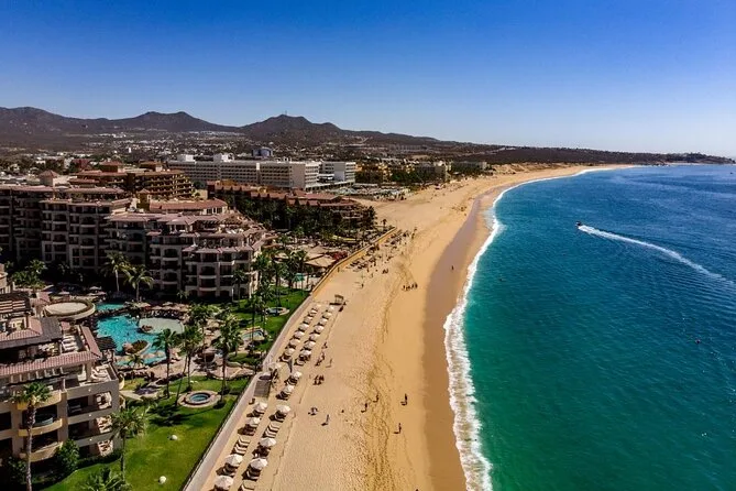 Aerial view of Médano Beach in Cabo San Lucas, a long curve of golden sand with beach umbrellas, resorts and calm blue water
