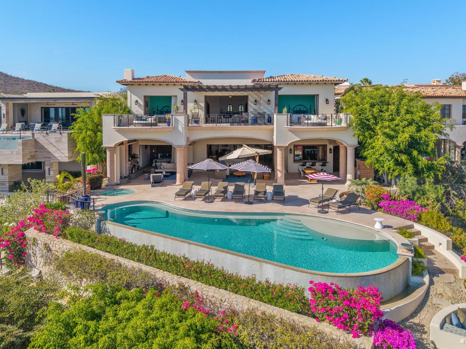 Two-story home with a long curved pool, lounge chairs and pink bougainvillea in Cabo del Sol, Los Cabos