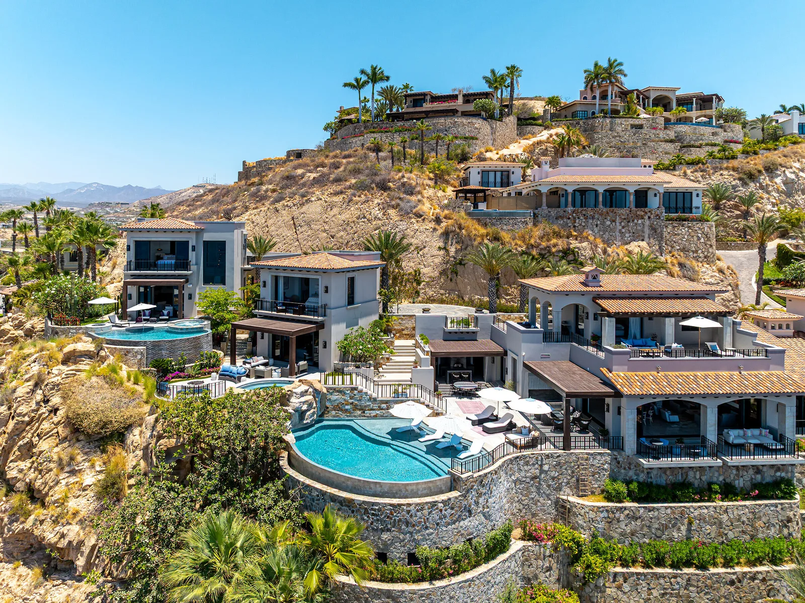 Terraced hillside homes with pools and palm trees in Palmilla on the Los Cabos Corridor, under a clear blue sky