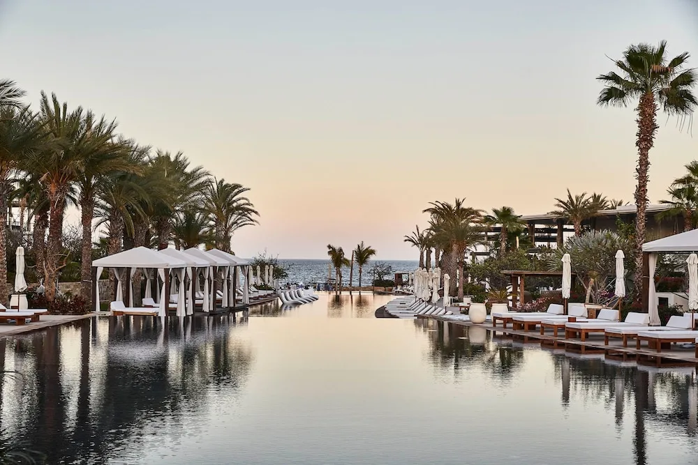Long infinity pool lined with palm trees and white cabanas at Chileno Bay Resort at sunset