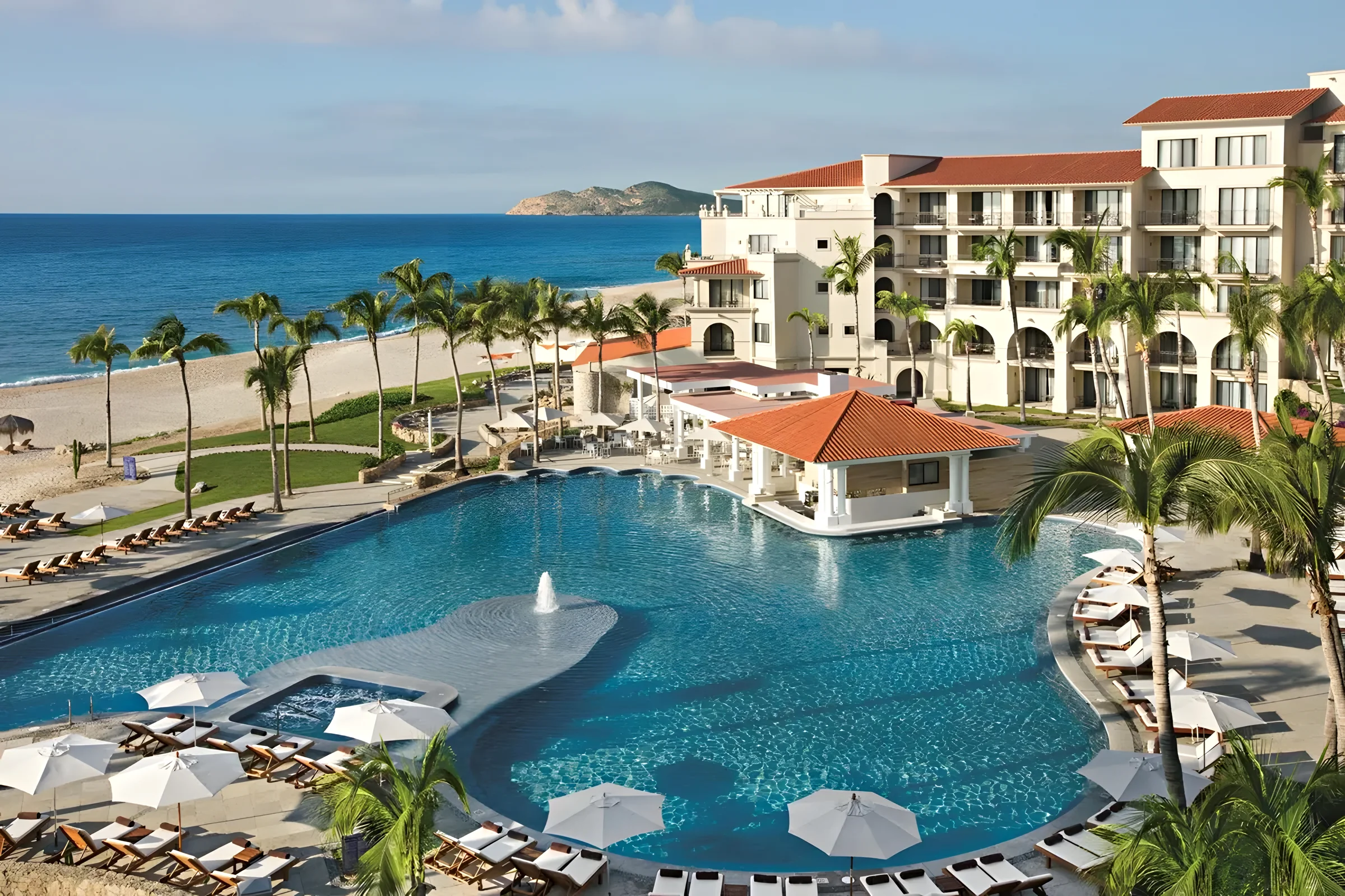 The large free-form pool at Dreams Los Cabos, with lounge chairs, palm trees and the beach and ocean behind it