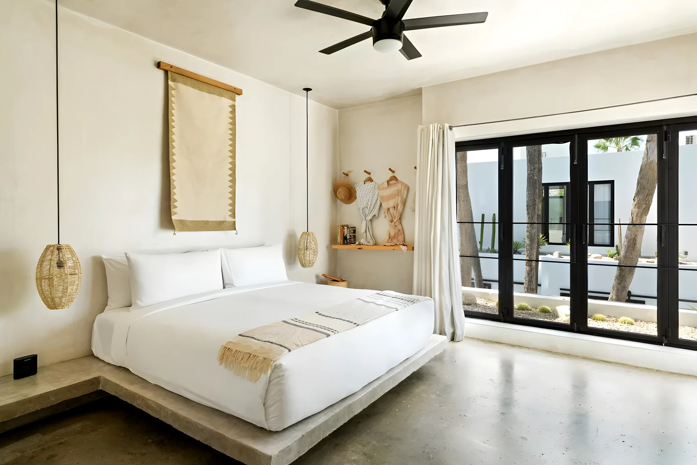 Bright guest room at Drift San José del Cabo with a low white bed, woven pendant lights and black-framed glass doors