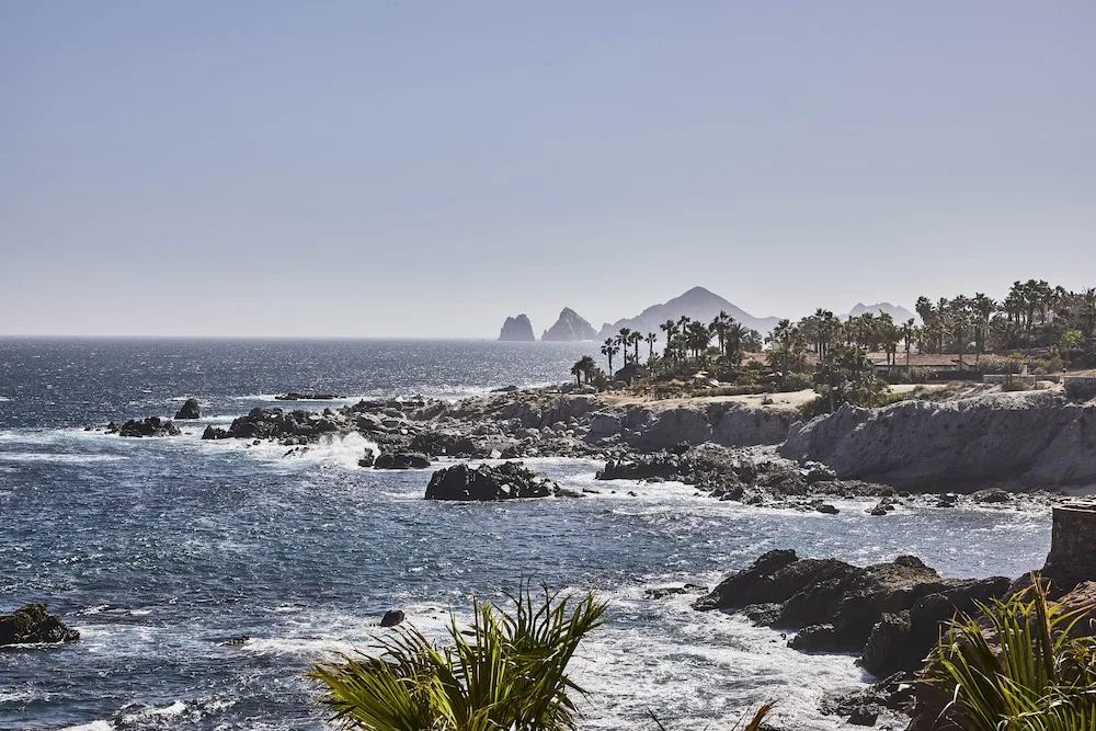 Waves breaking on the rocky coastline in front of Esperanza, with Land's End rock formations in the distance