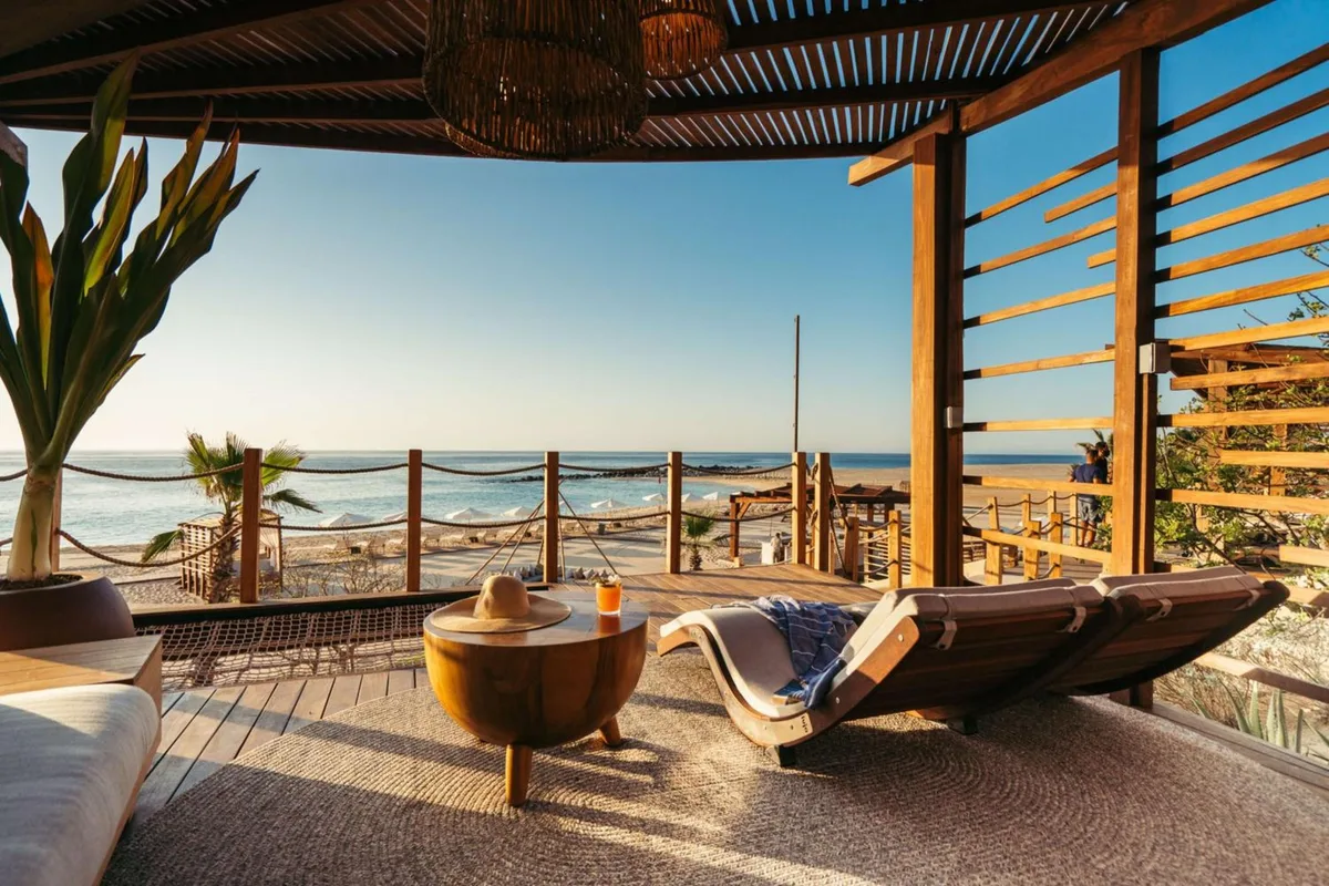 A shaded wooden beach deck with a lounger at Hilton Los Cabos, looking out at the sand and the ocean