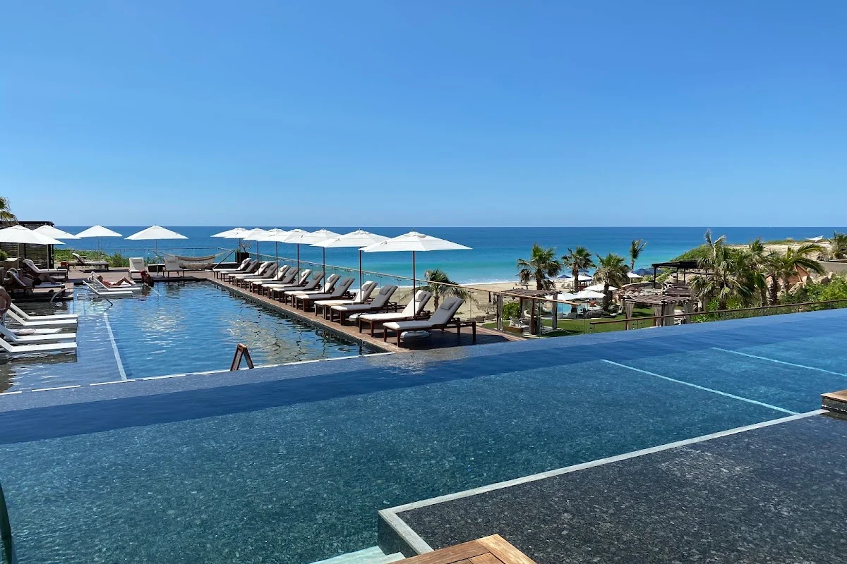 Zadún infinity pool lined with white umbrellas and loungers above the beach in Puerto Los Cabos
