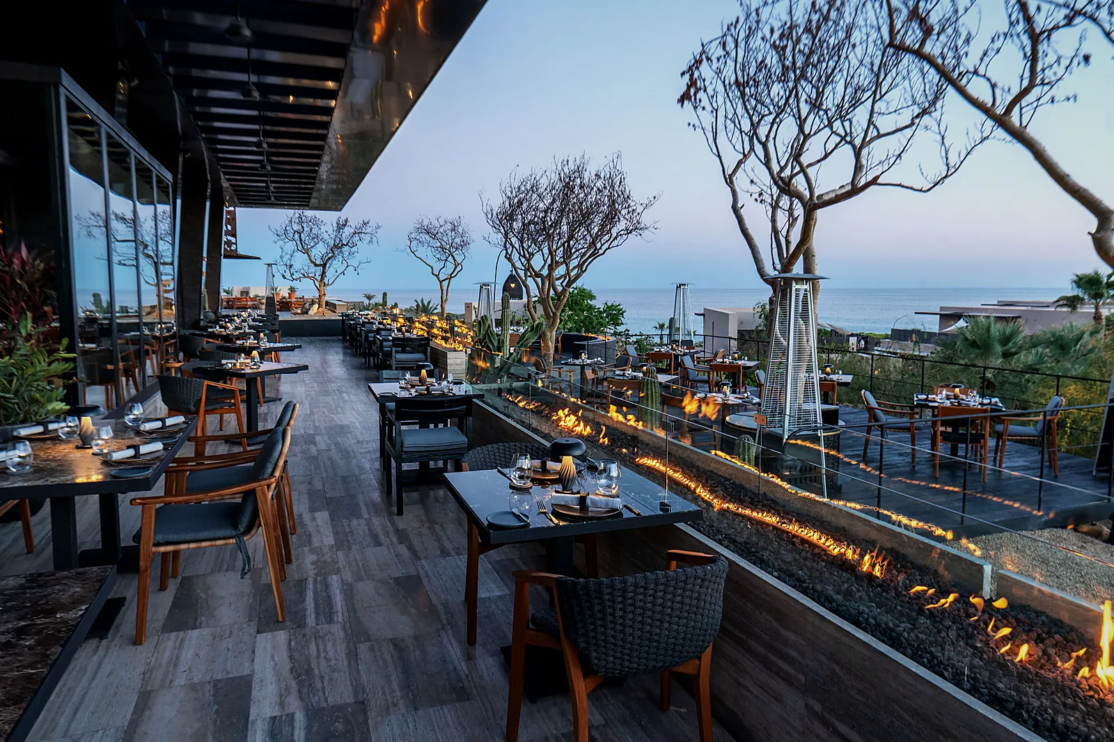 Terrace tables at HUMO at Zadún with a long lit fire feature and the Sea of Cortez at dusk