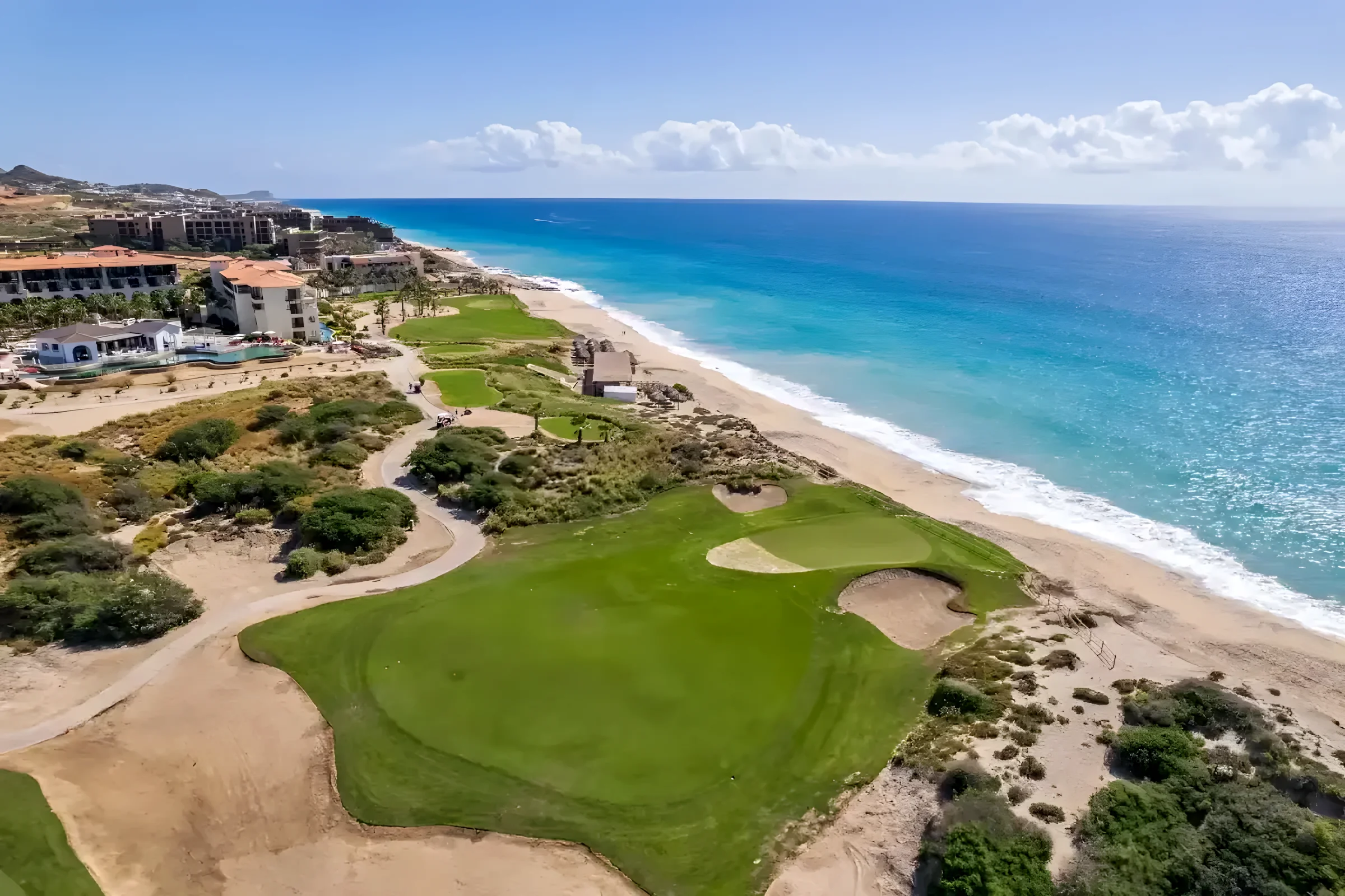 Aerial view of a green and bunkers at Puerto Los Cabos, right next to a sandy beach and the blue Sea of Cortez