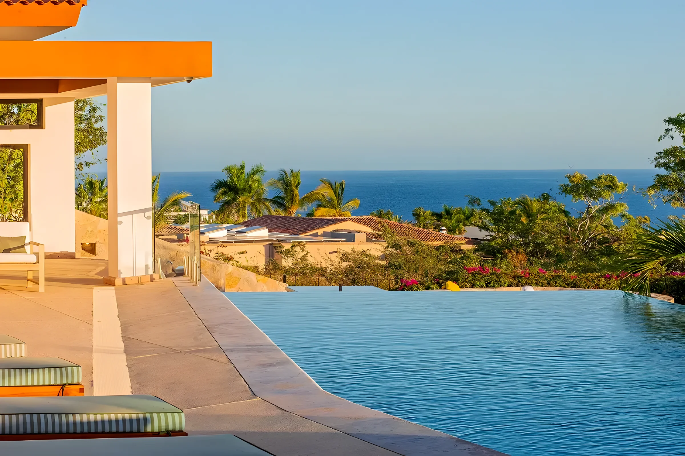 Casa Primavera infinity pool in Puerto Los Cabos with its edge facing palm trees, rooftops and the blue ocean on a clear day