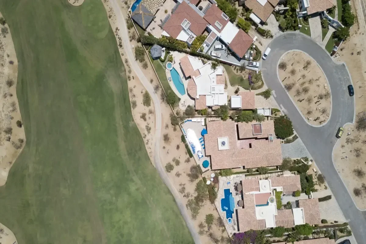 Top-down view of tile-roof homes with private pools lined up along a fairway in Cabo del Sol