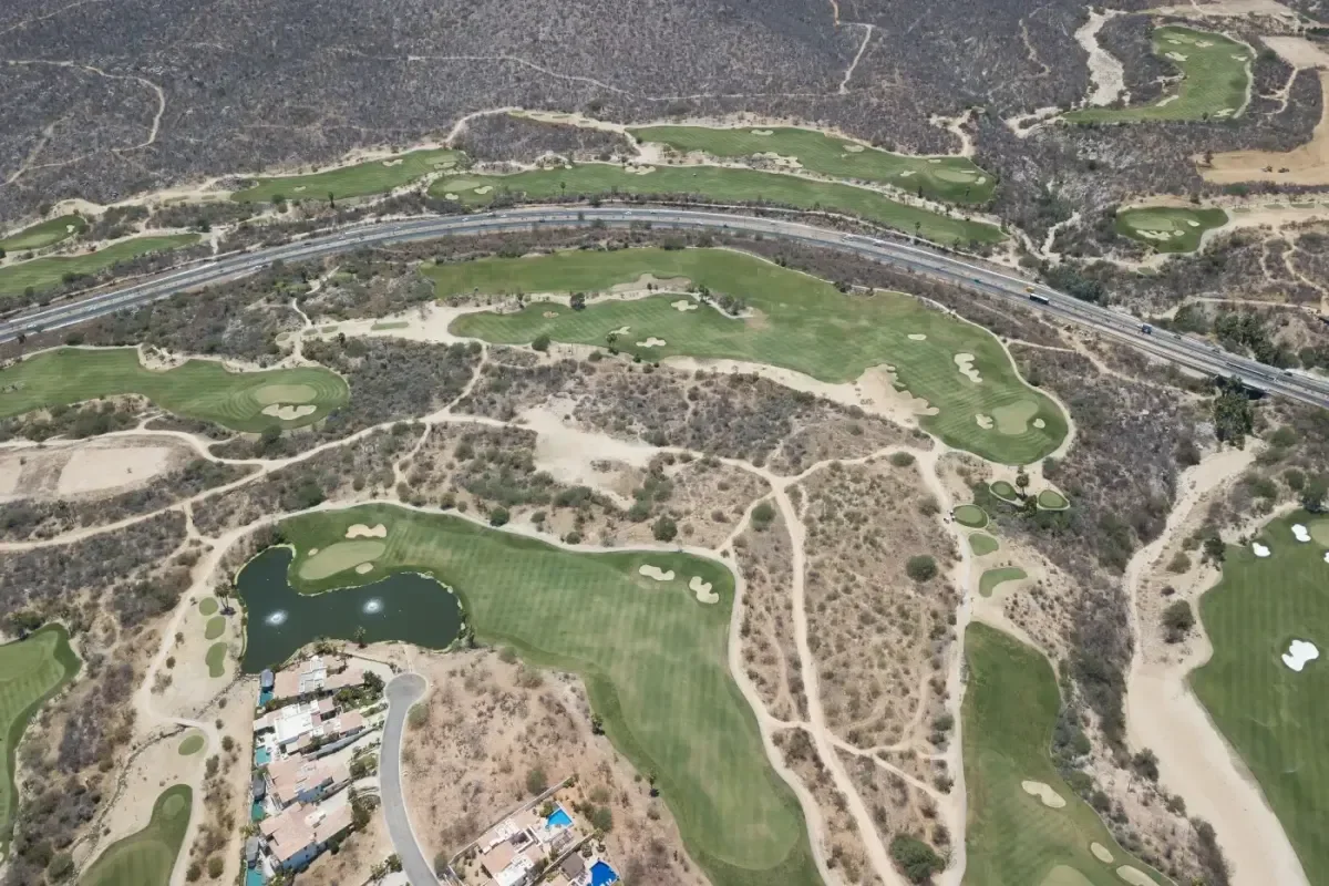 Aerial view of green fairways, a pond and homes cut into the desert at Cabo del Sol, with the highway and more golf holes behind
