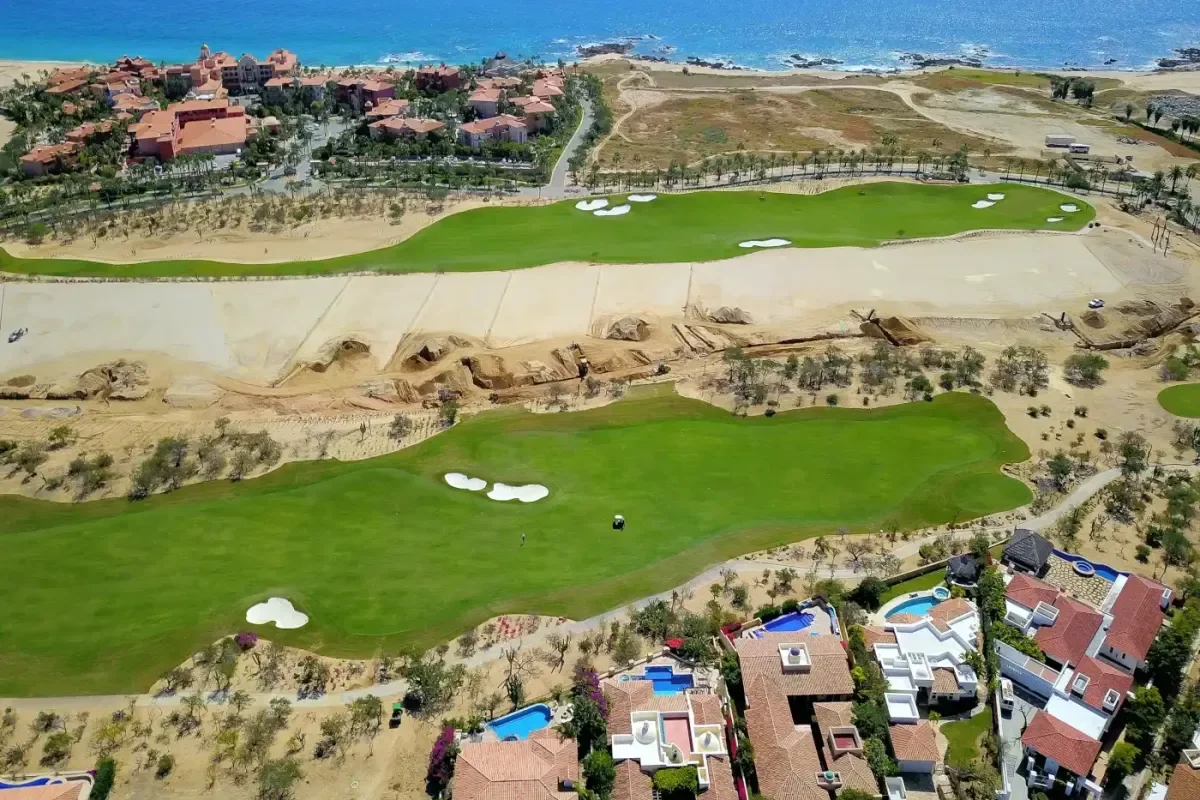 Aerial view of two green fairways with white sand bunkers in Cabo del Sol, with villas in front and the ocean behind
