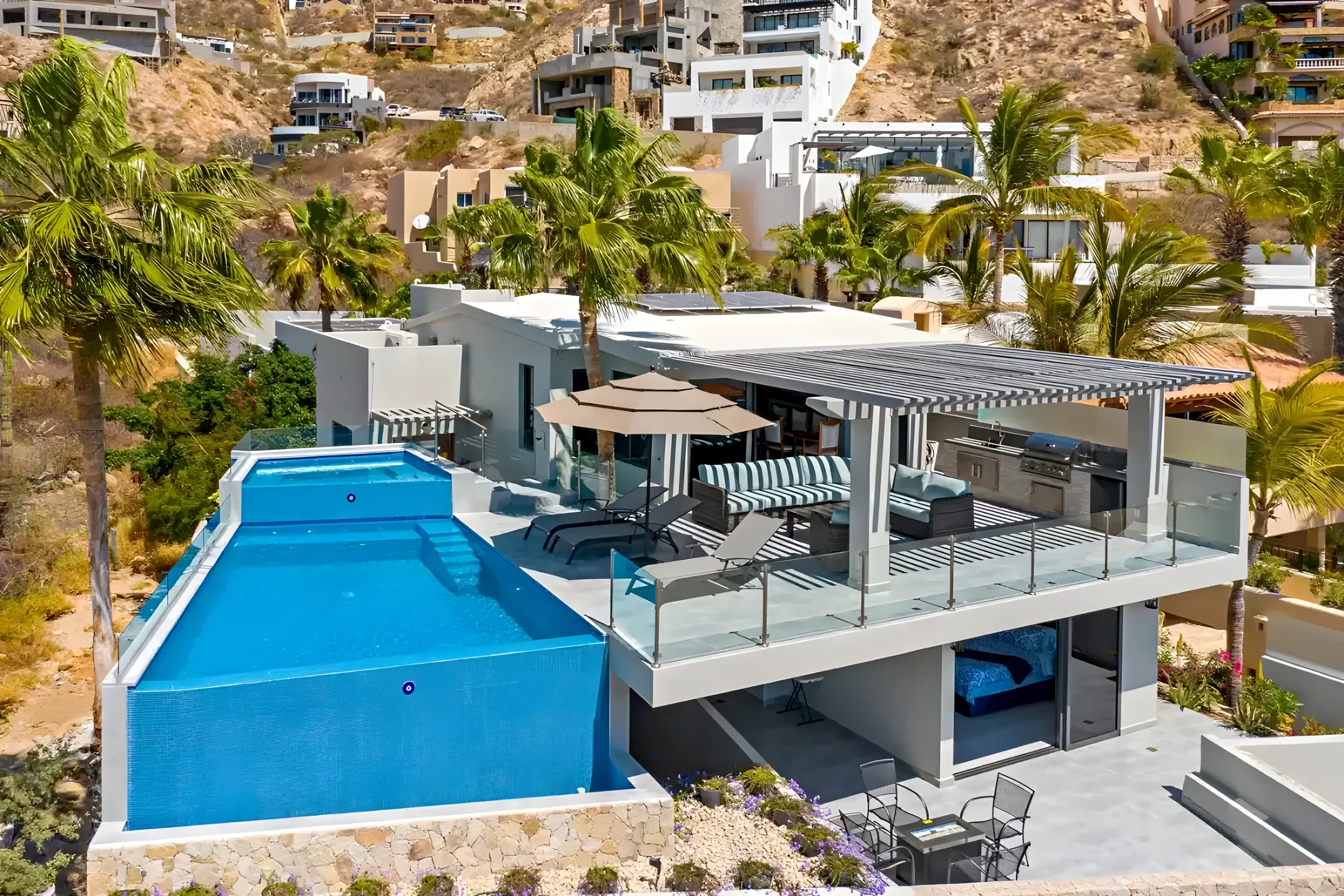 Aerial view of Villa Nazar in Pedregal showing a raised infinity pool beside a covered terrace with outdoor lounge seating and palm trees