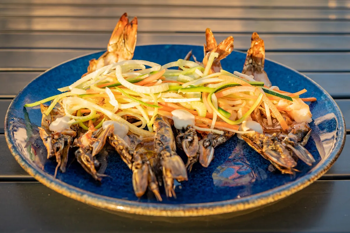 Grilled prawns topped with shaved vegetables on a blue plate at Sunset Monalisa